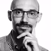 Ein Mann mit Brille und gestreiftem Hemd schaut nachdenklich in die Kamera und stützt sein Kinn mit der Hand.