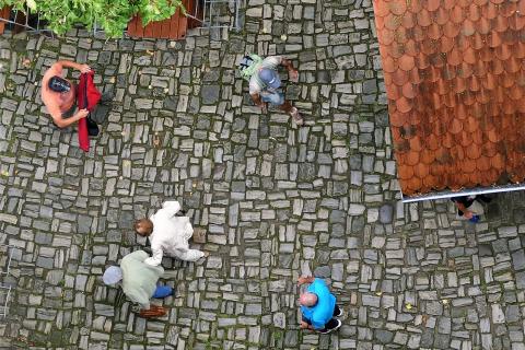 Overhead view of five people walking on a cobblestone street, one holding a red blanket and another carrying a green bag.